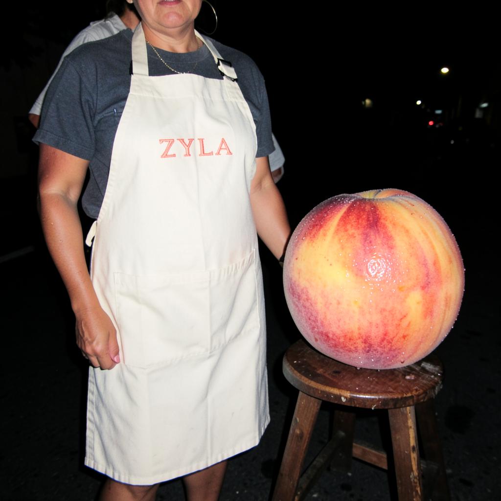 Cream ZYLA sampling apron worn next to a giant peach on a stool